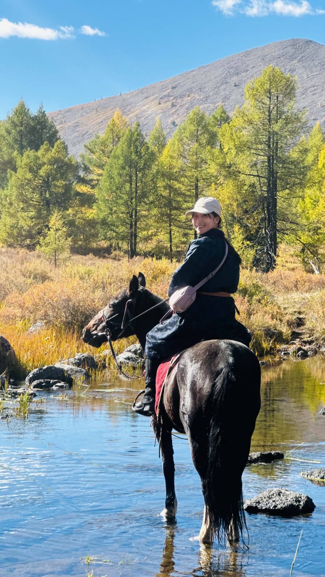 A guest looking back from the saddle while her horse stands in the river