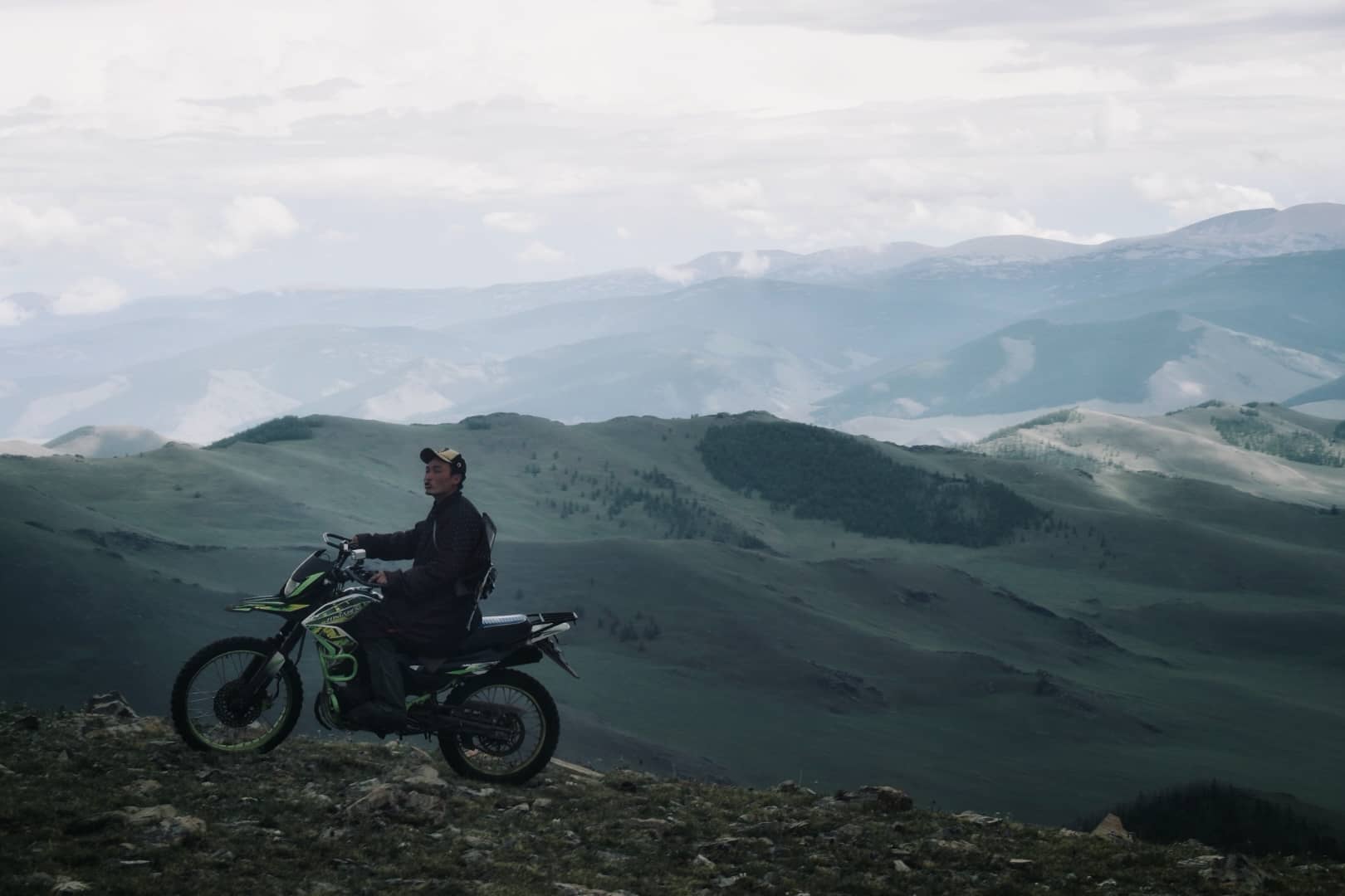 A herder on a motorbike pausing on a ridge above the green valleys