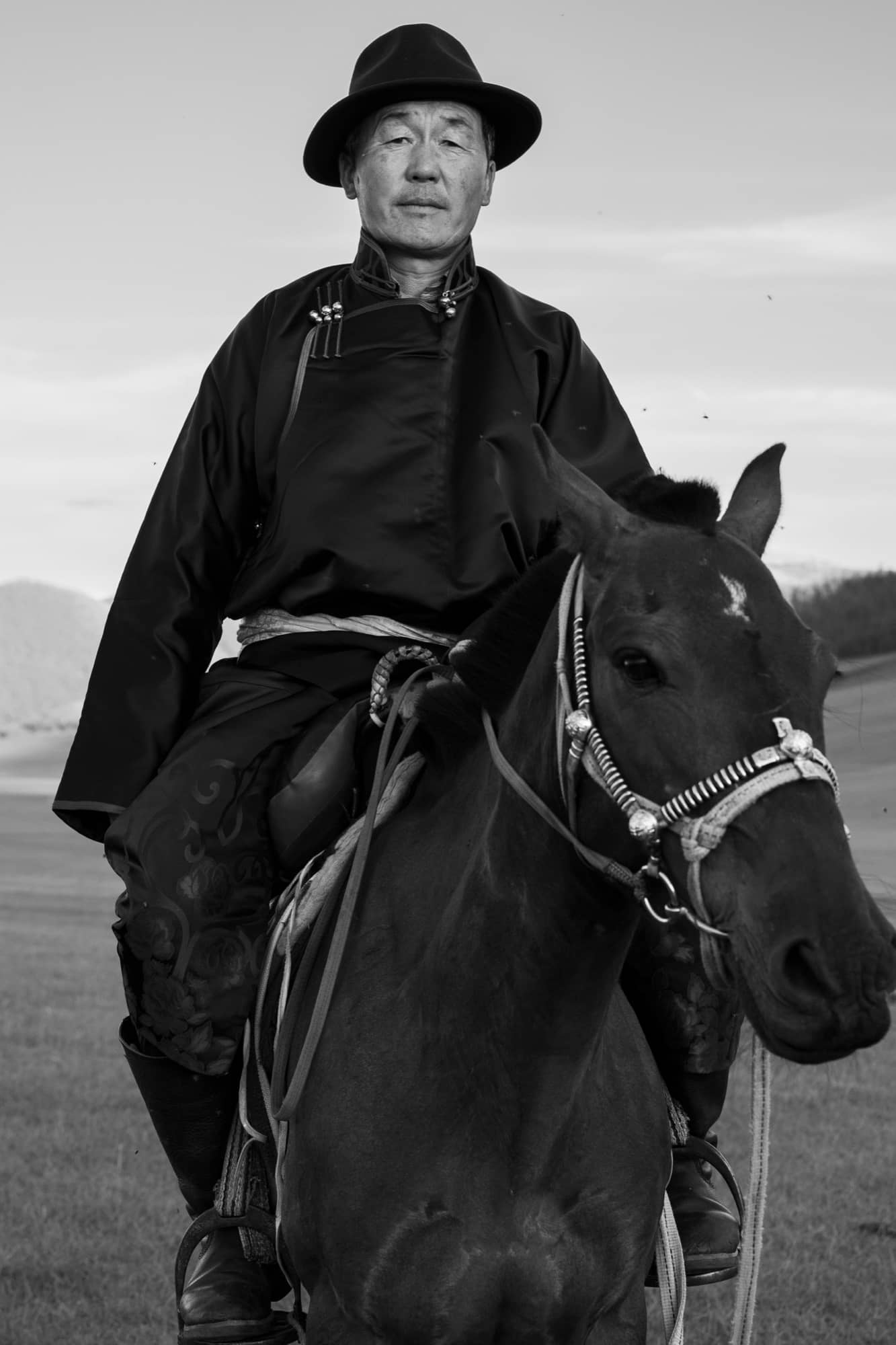 A horseman in a deel and hat mounted on his dark horse, in black and white