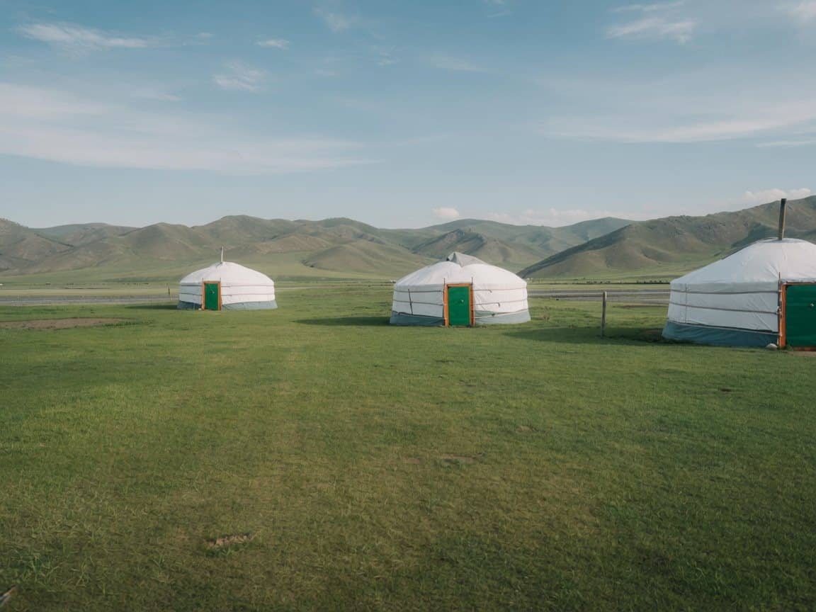 White gers spread across open grassland below the mountains