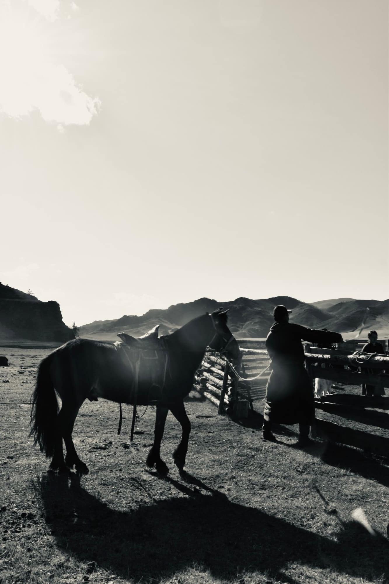 Saddling up at the corral in the morning light, in black and white