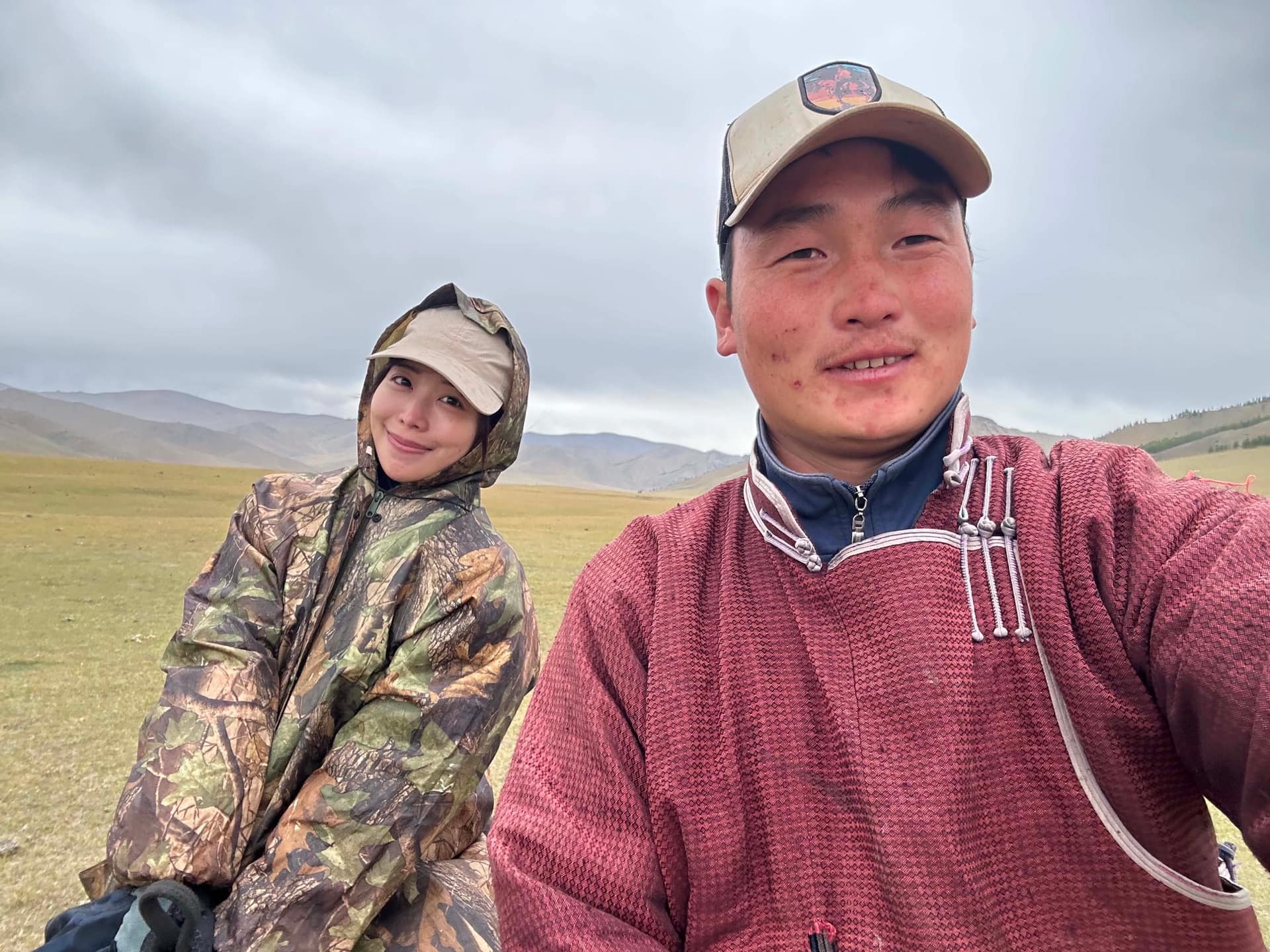 A guest in rain gear and the guide in a deel on the open steppe under heavy cloud