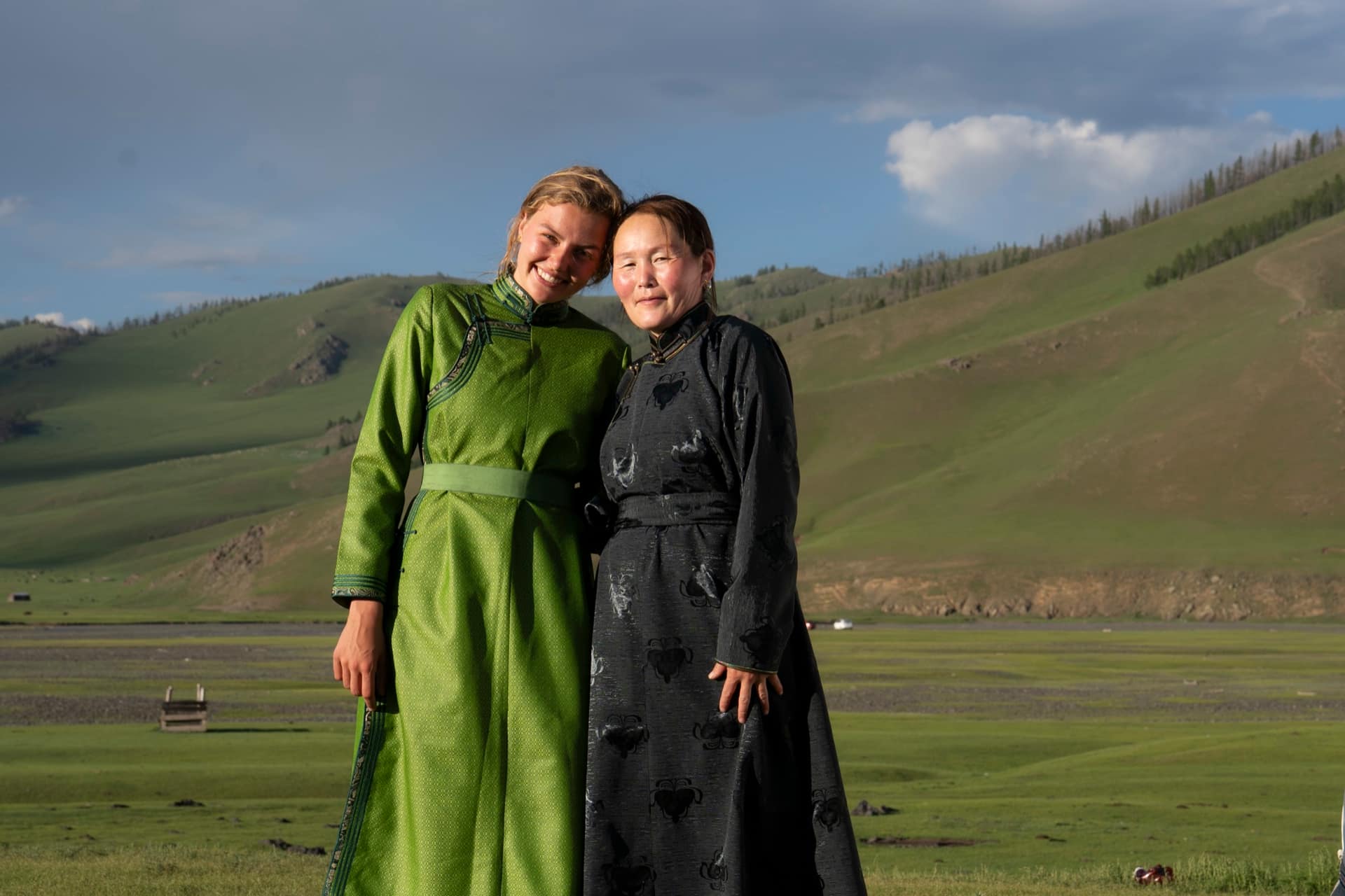 A guest and her host in traditional deels below the green hills