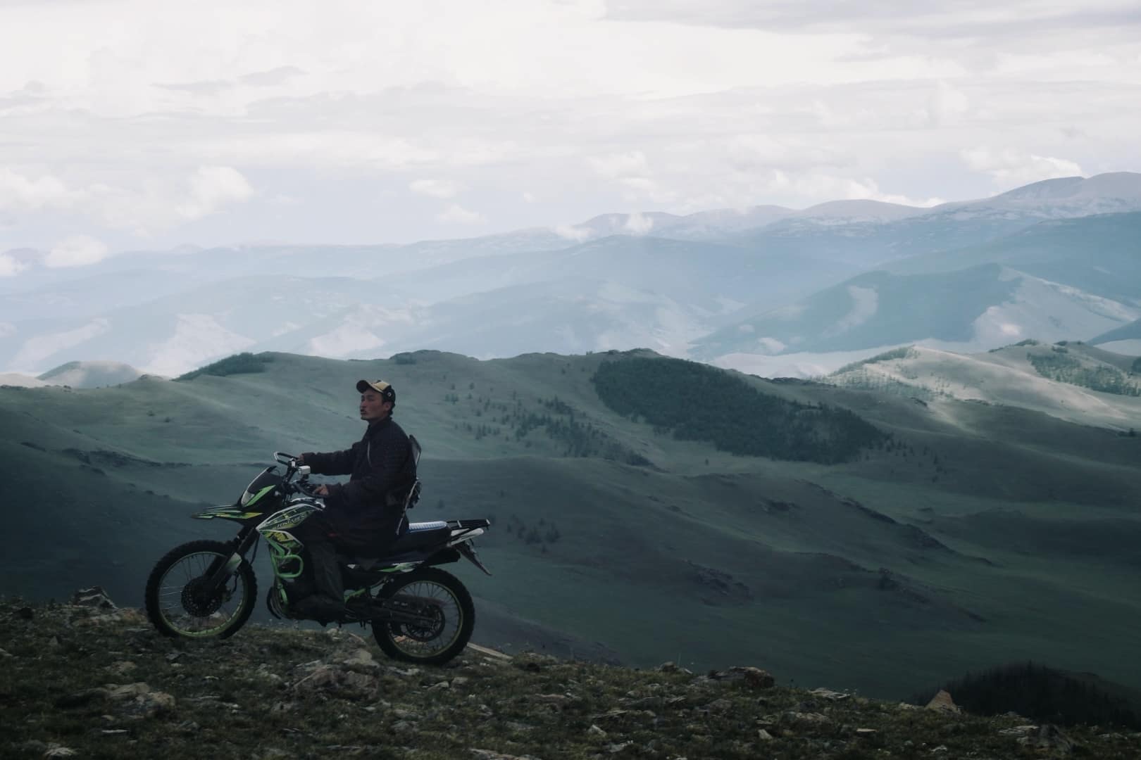 A herder on a motorbike pausing on a ridge above the green valleys
