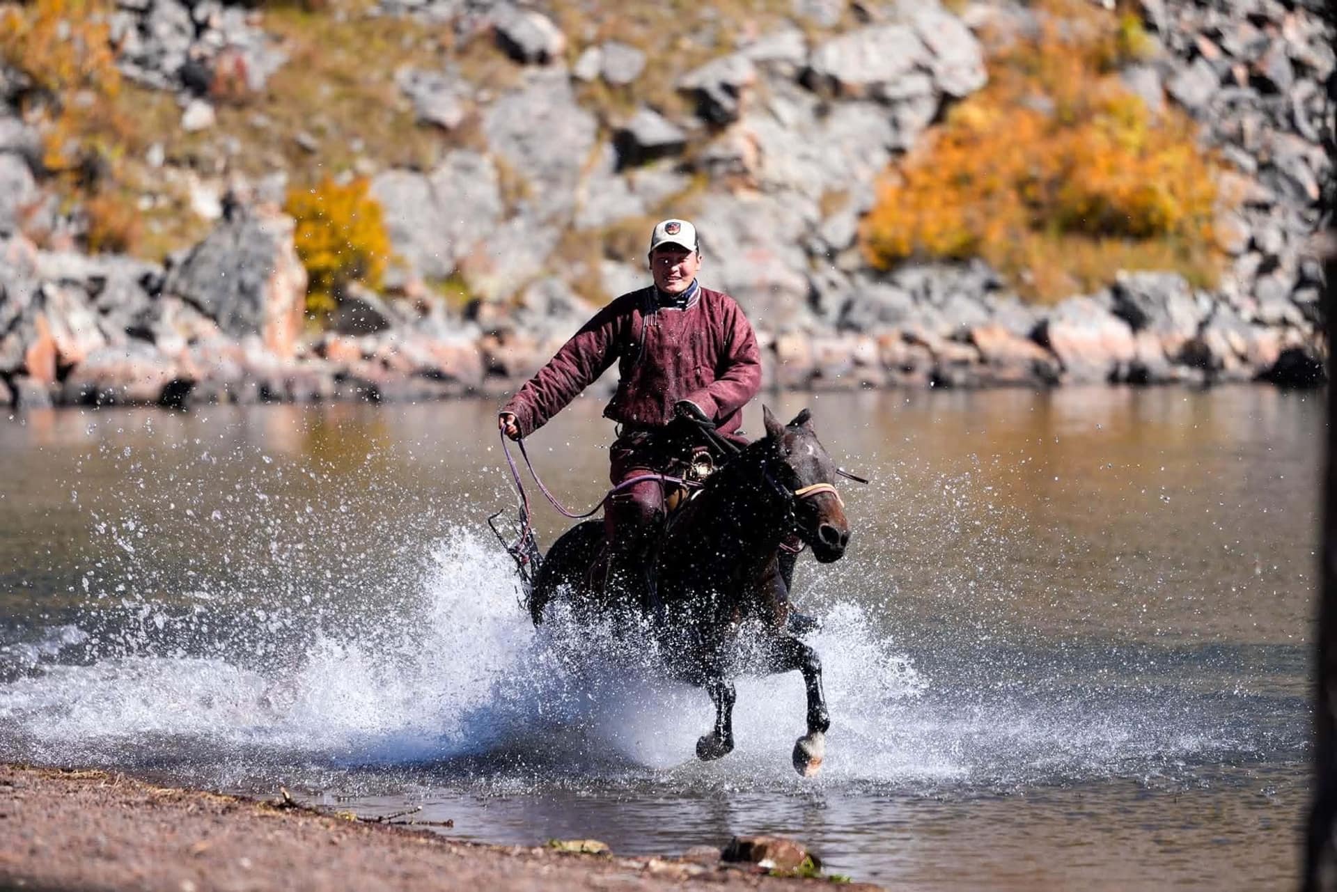 A horseman galloping through the river in a burst of spray below autumn rock