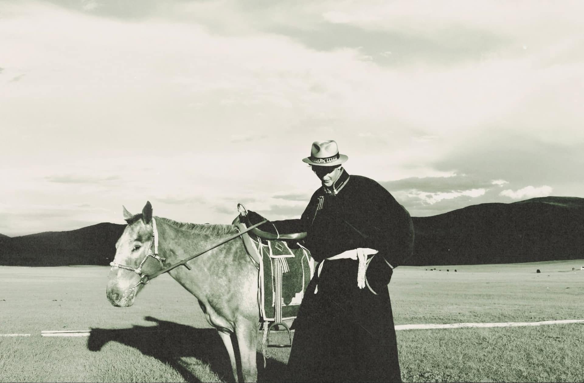 Horseman in a deel and straw hat beside his saddled horse, shot on film