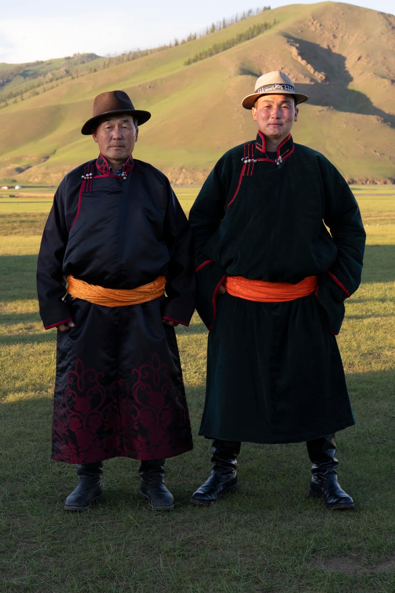Father and son in dark deels with orange sashes on the summer steppe