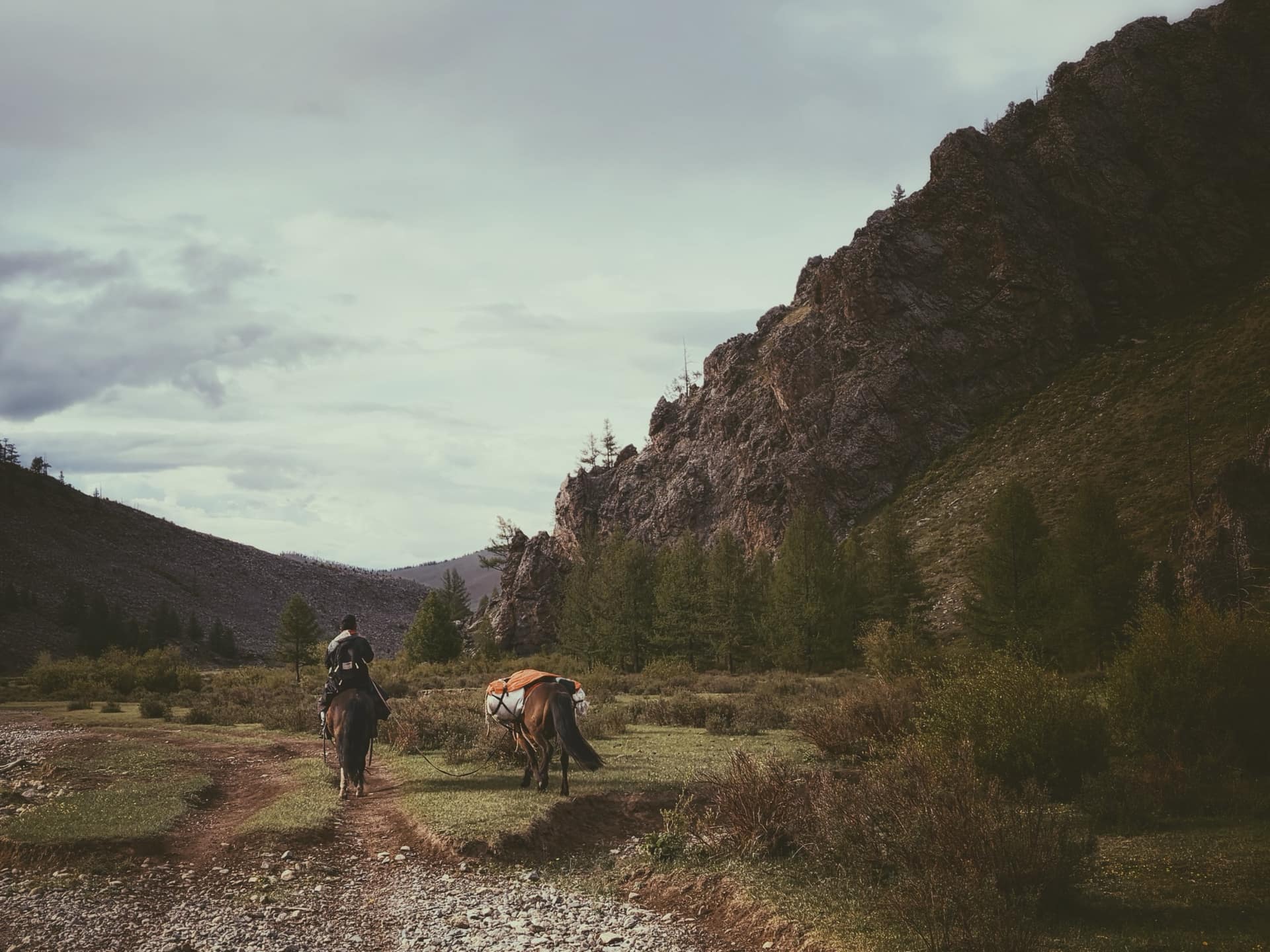 A rider leading a loaded pack horse along the valley track below the cliffs
