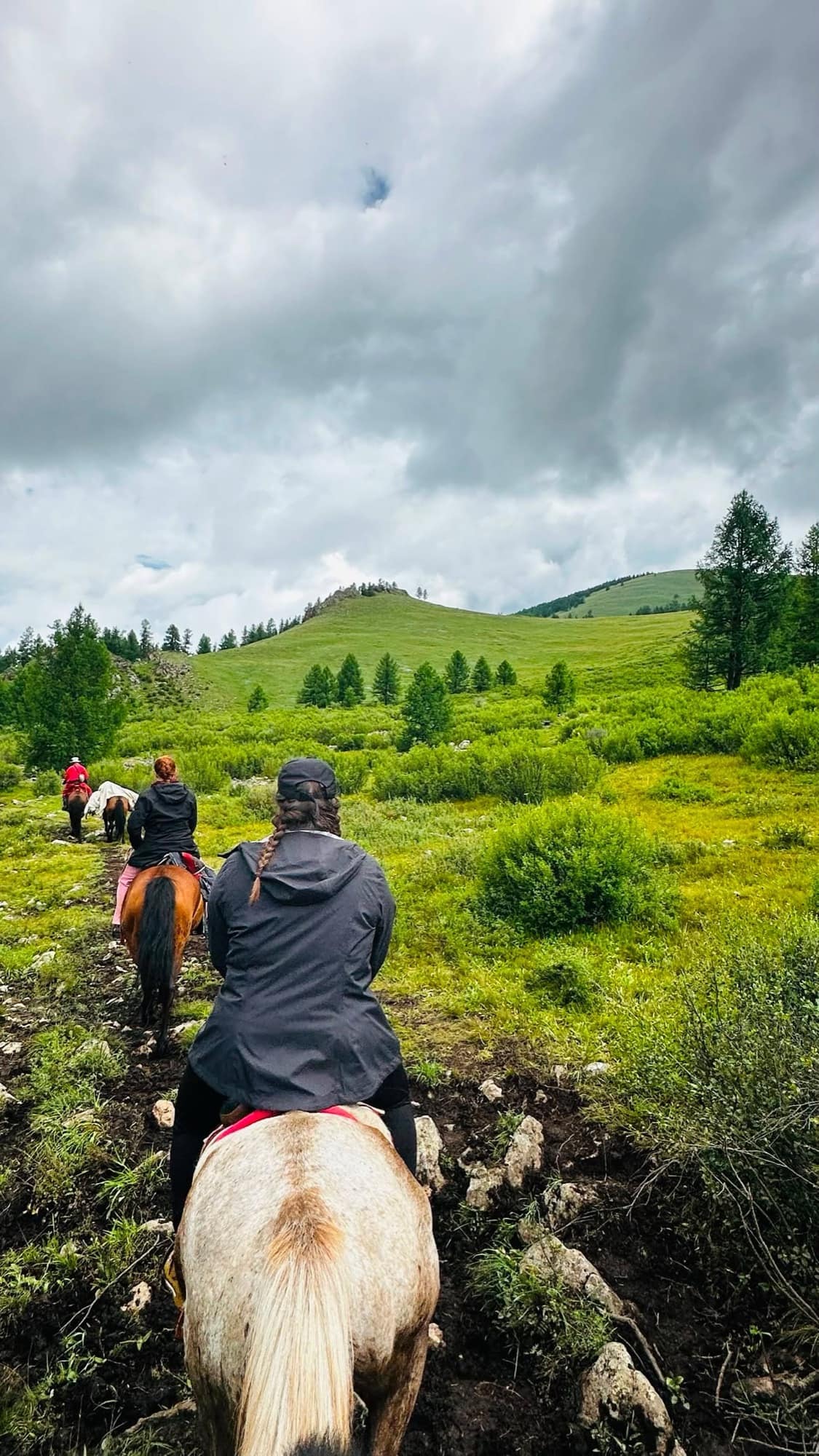 Riders climbing a green hillside under heavy cloud