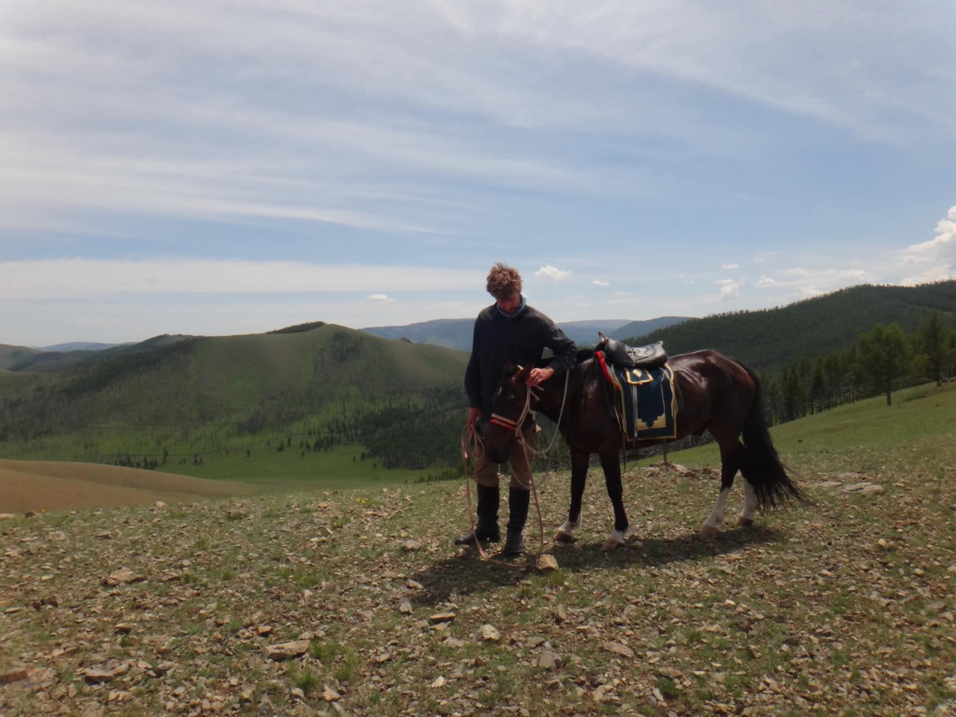 Checking the saddle on a ridge above green hills