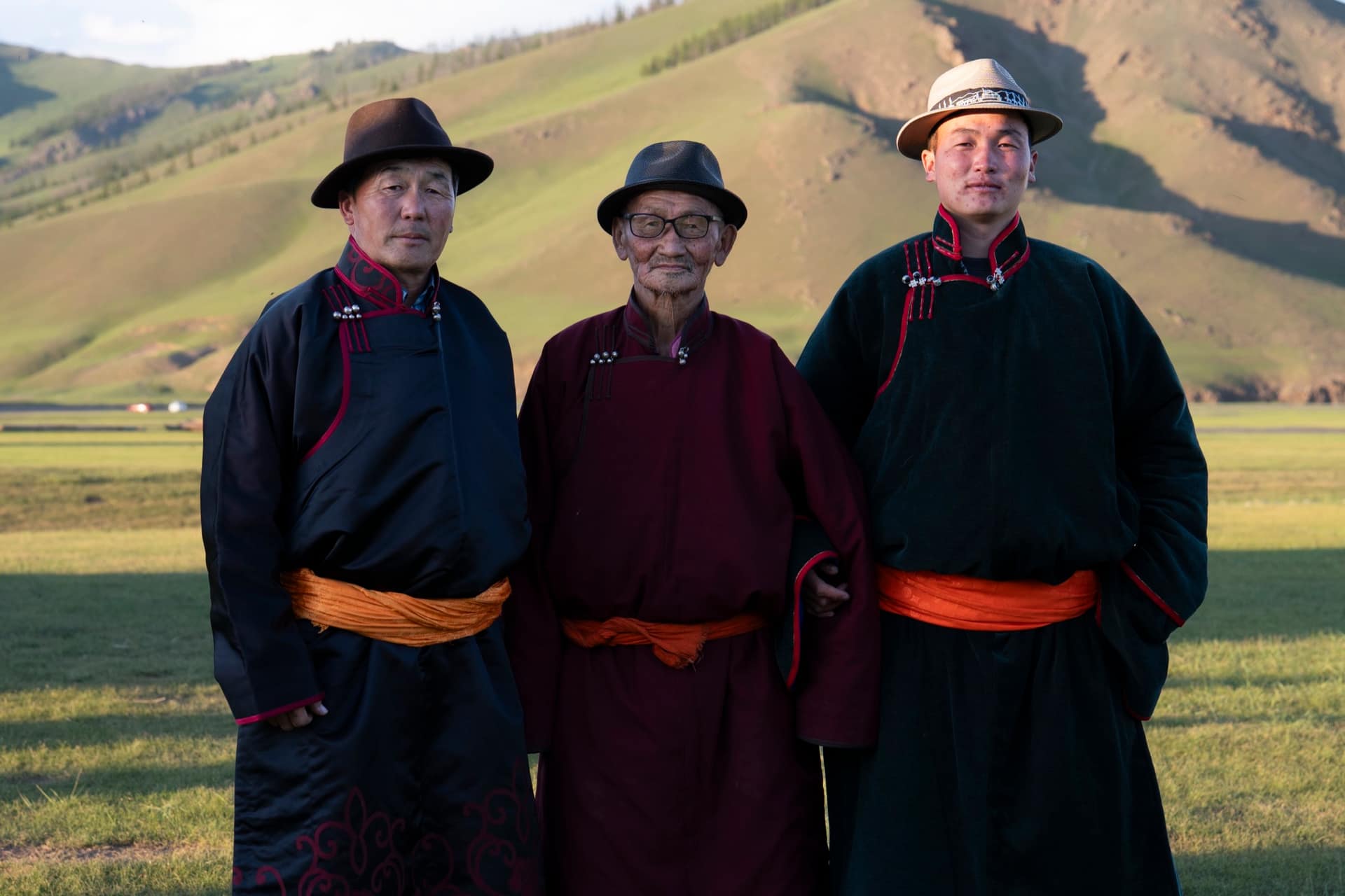 Three men of the host family in traditional deels and hats below the green hills