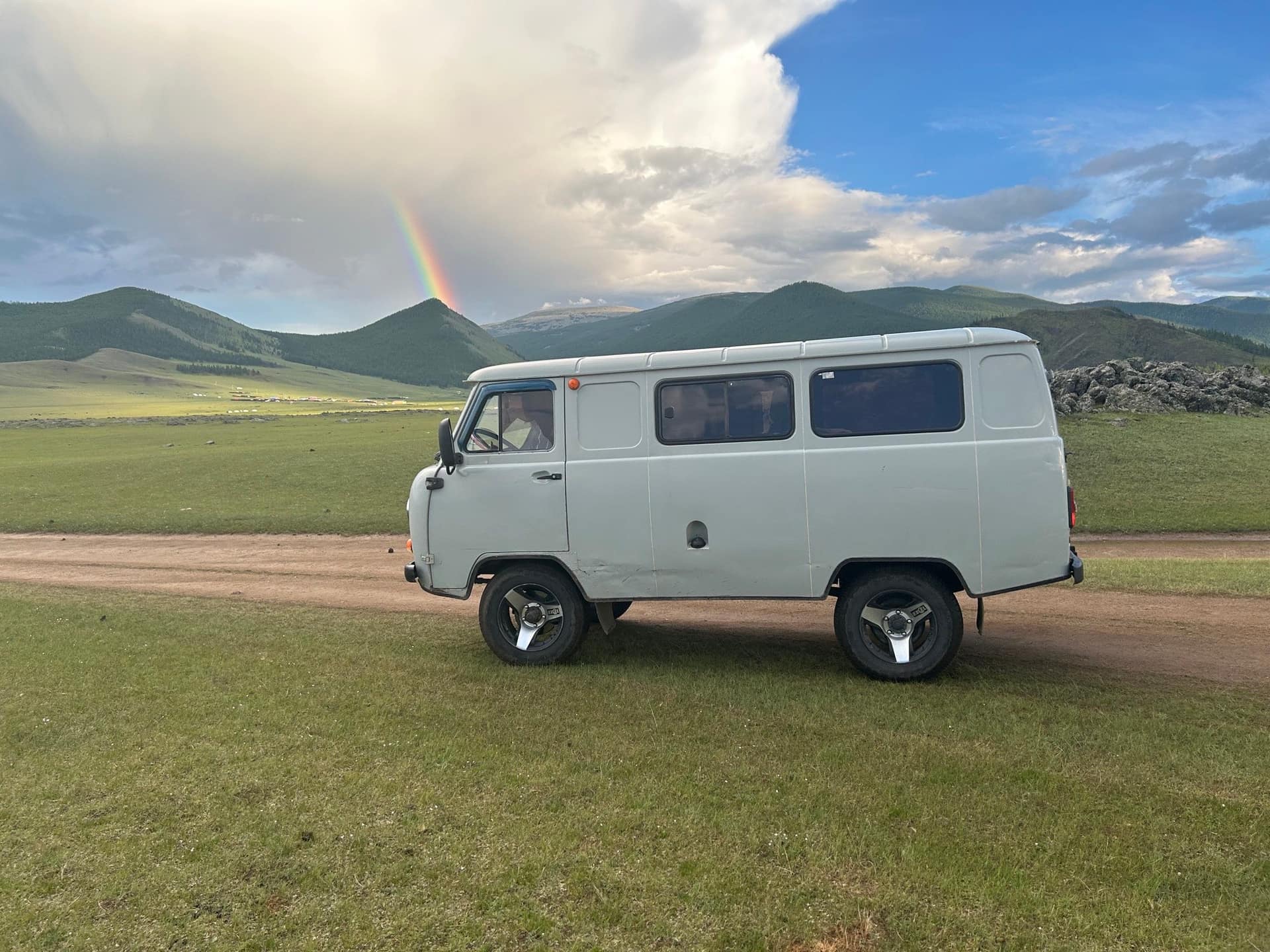 The van on the steppe track under a rainbow