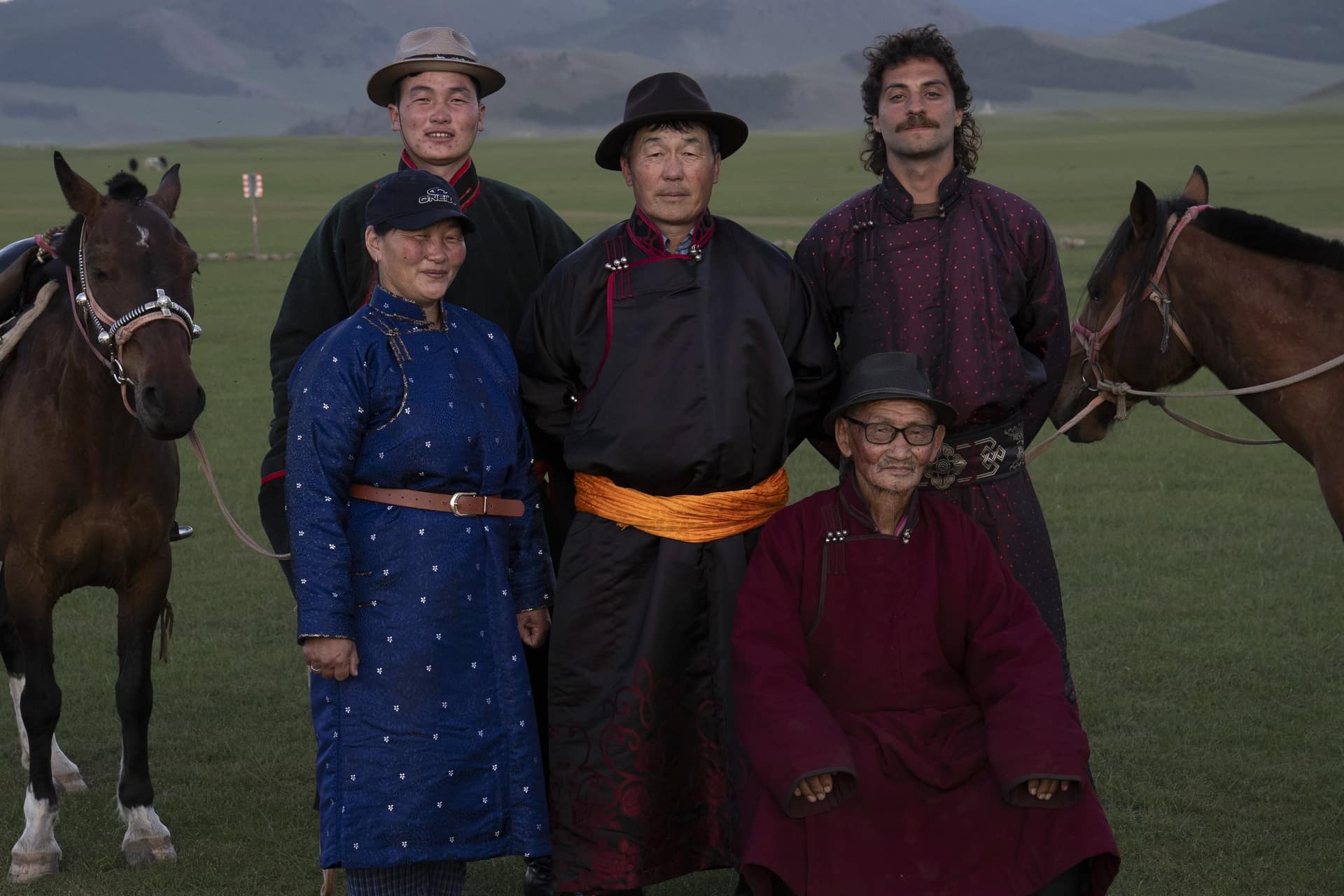 Robert with the host family in traditional deels, two of their horses beside them on the steppe